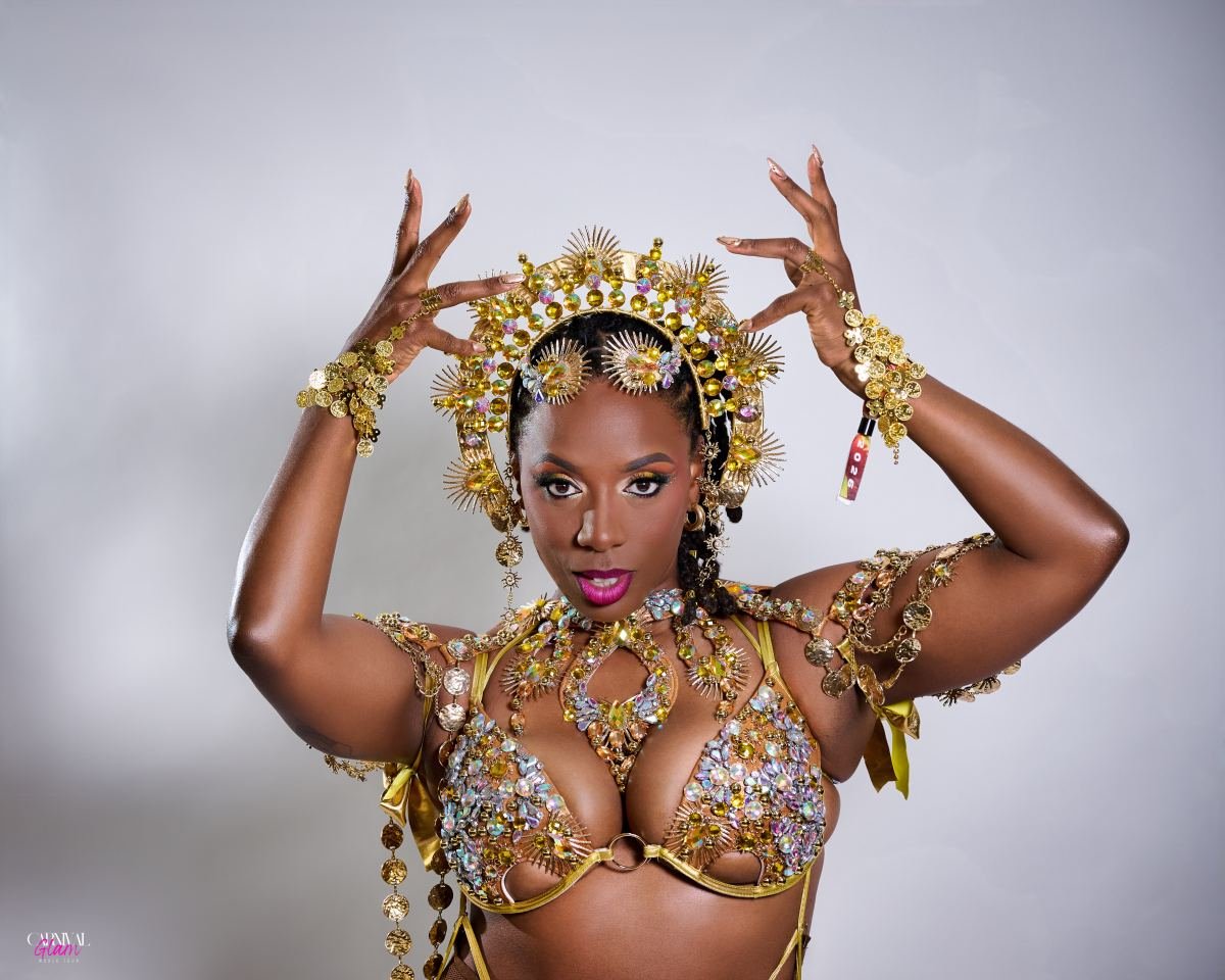 Massinda Zinga in a jewelled gold carnival costume and sunburst headdress, hands raised above her head