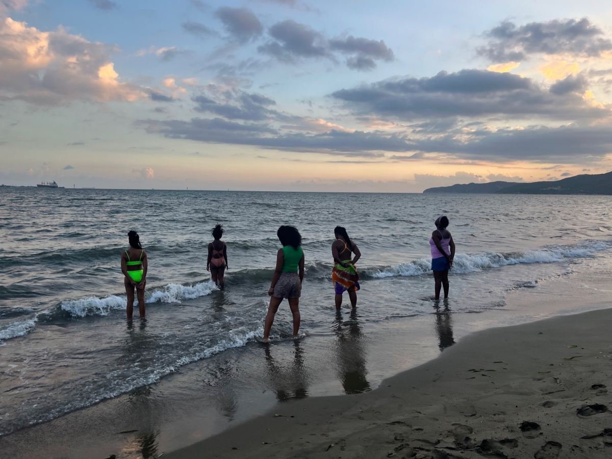 Five women stepping into the sea at sunset