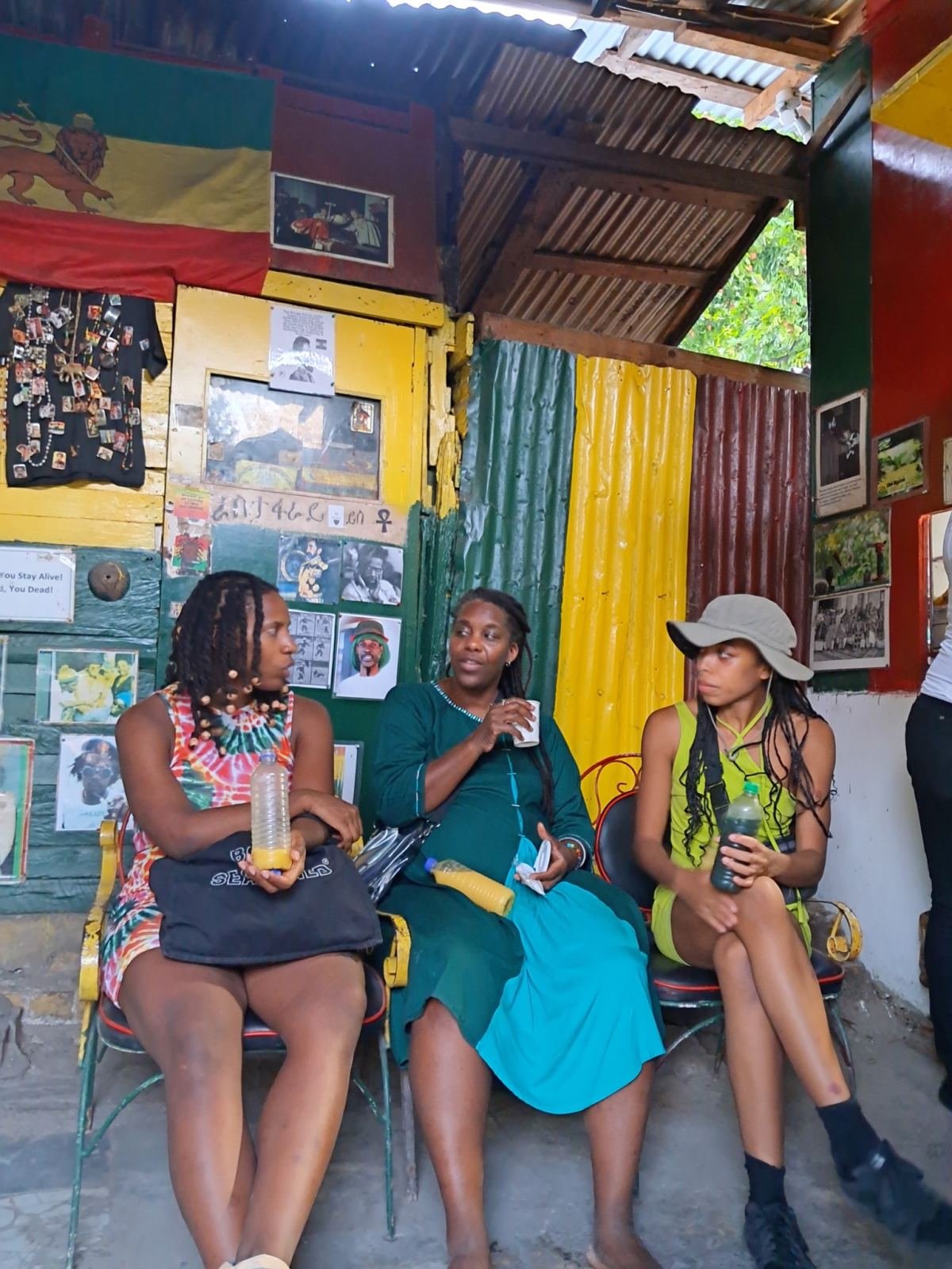 Three women sitting together in a colourful yard hung with photographs