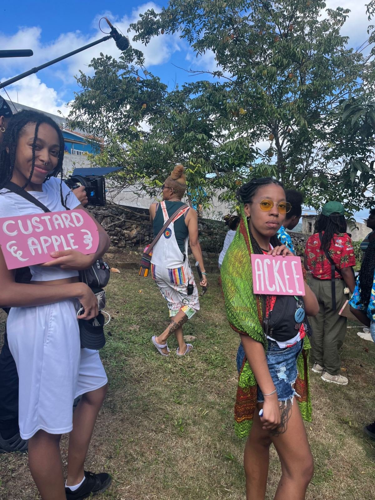 Women at an outdoor gathering, one holding a “Custard apple” sign