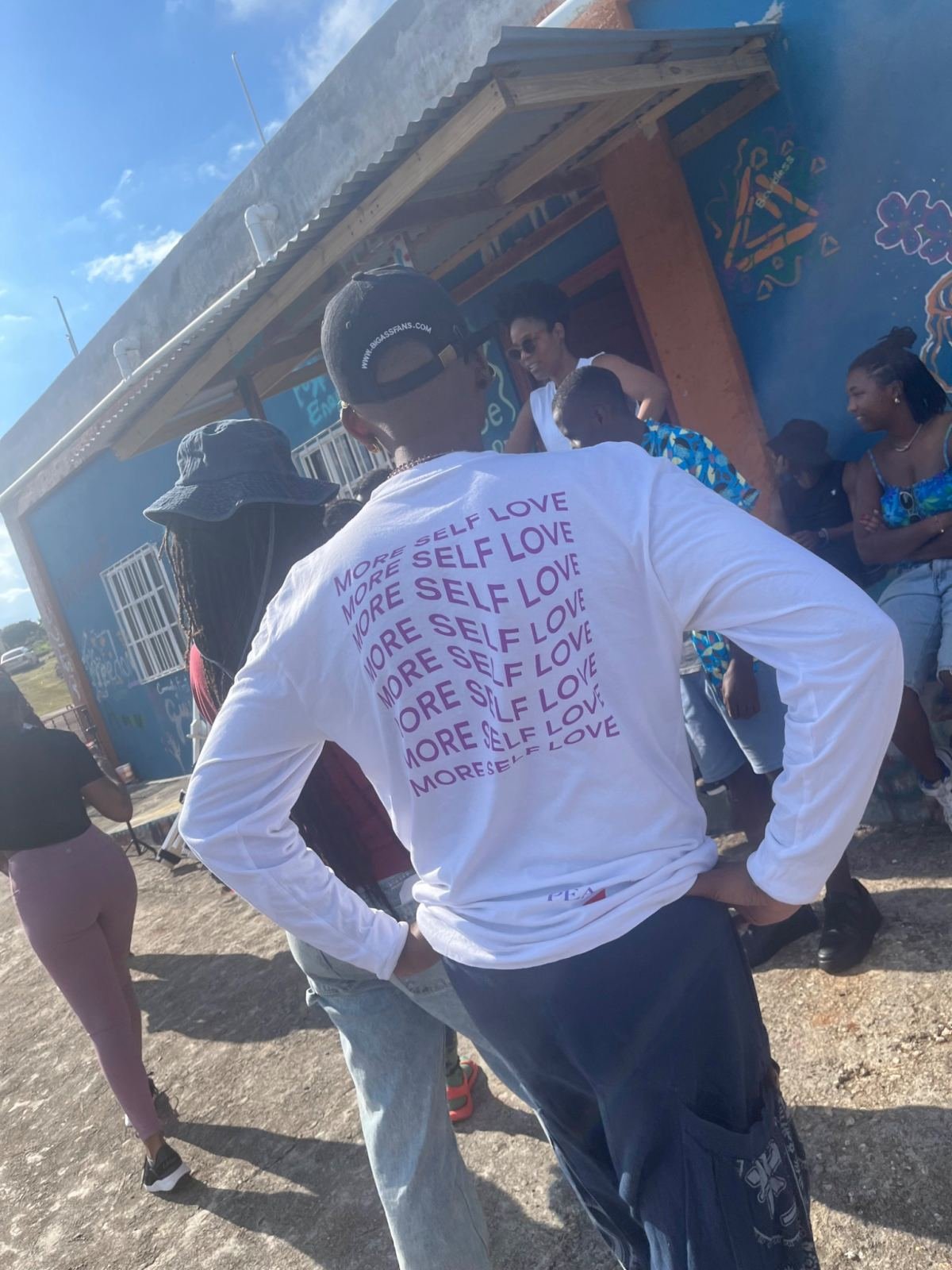 A man in a “More self love” shirt among the group outside a painted building