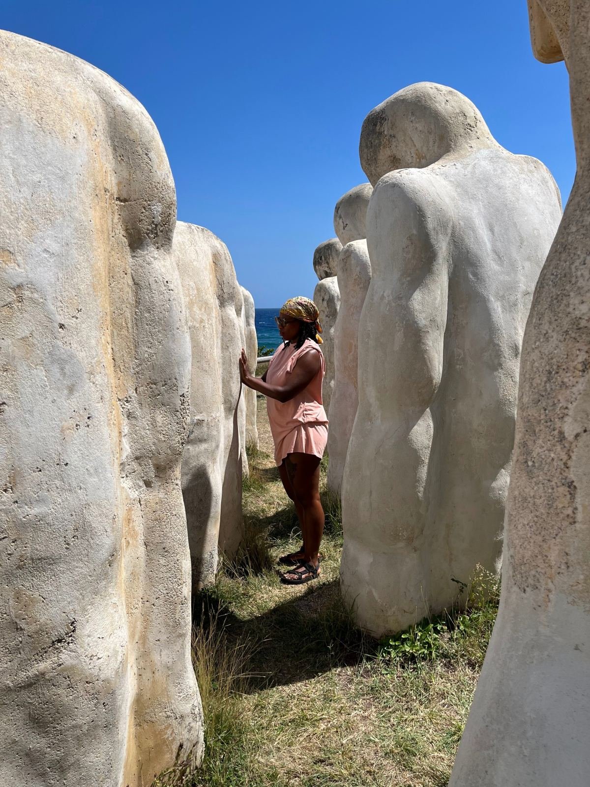 A woman among the tall white stone figures of the Cap 110 memorial at Anse Caffard, Martinique